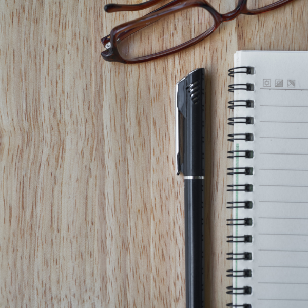 A pen and a pair of glasses placed next to a notebook.